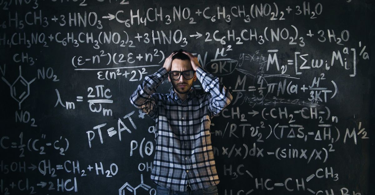 Man in glasses focusing on math problems, struggling with complex equations on chalkboard.